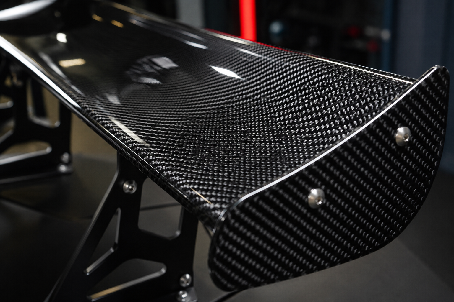 Detailed macro image of a carbon fiber wing surface with glossy clear coat, tight carbon weave pattern, mounting brackets, and workshop lighting for a luxury sports car part